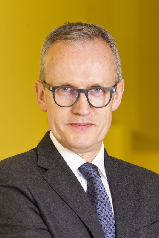 A man in glasses and a suit with his arms folded, displaying confidence and professionalism.
