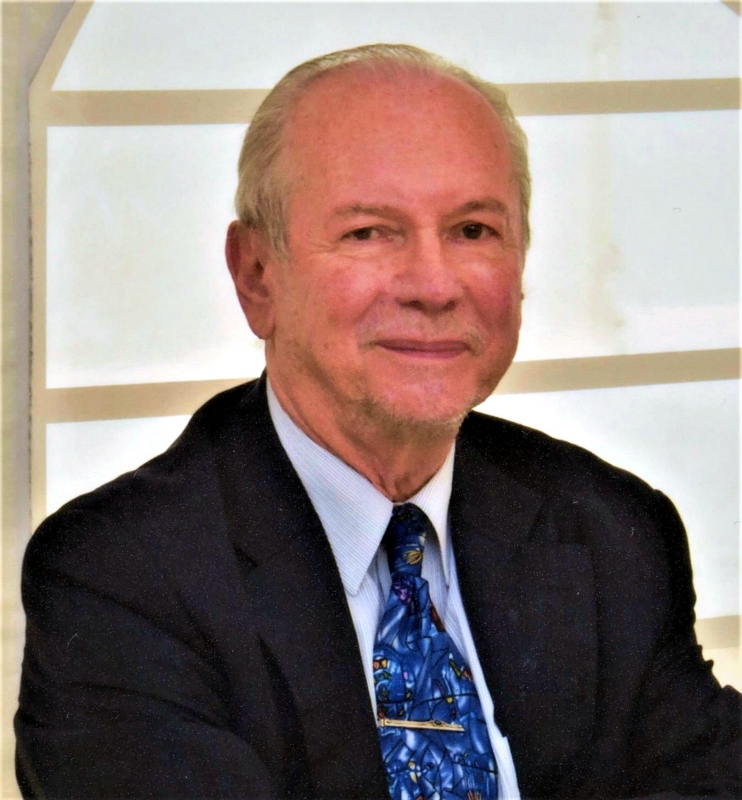 A man in a suit and tie sits in front of the window, presenting a professional image.