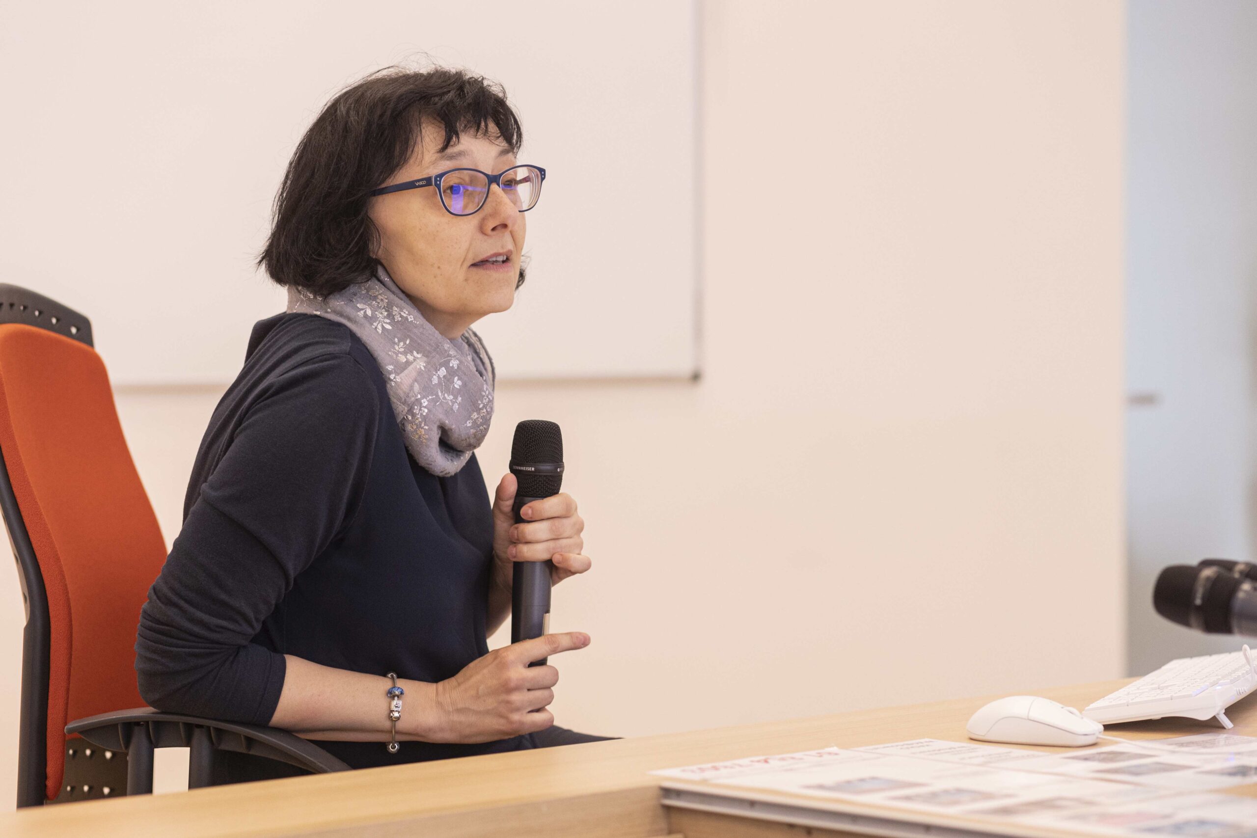 A woman sitting at a table with a microphone, ready to speak or record.