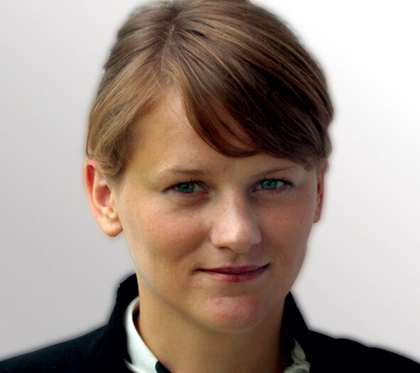 A woman with short brown hair smiles softly, showcasing her confident and approachable demeanor in a bright setting.