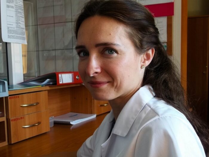 A woman in a white lab coat is seated at a desk, engaged in her work with focused concentration.