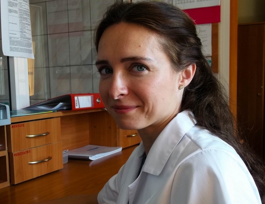A woman in a white lab coat is seated at a desk, engaged in her work with focused concentration.