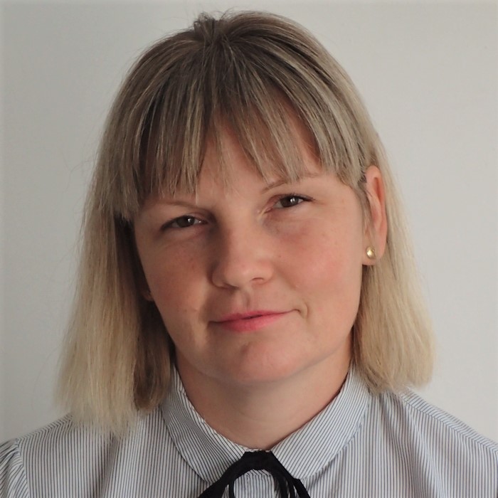 A woman with shoulder-length blonde hair, wearing a striped blouse and a calm expression.