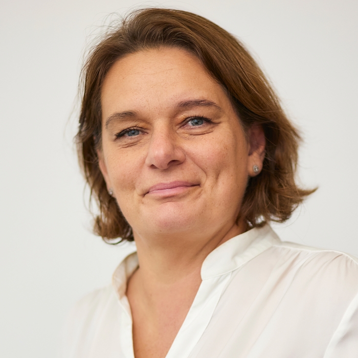A mature woman with a warm smile, wearing a white blouse, posed against a neutral background.