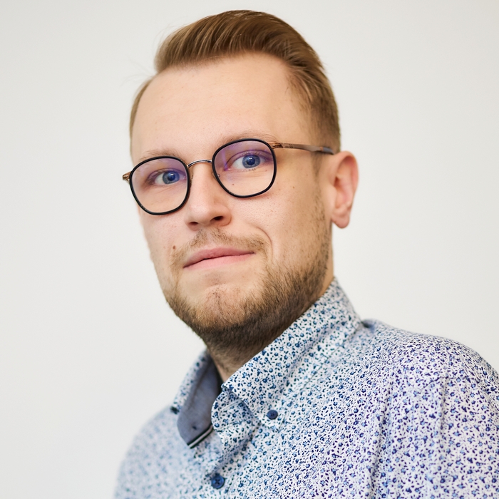A man with blond hair, wearing round glasses and a patterned shirt, looking off to the side with a thoughtful expression.