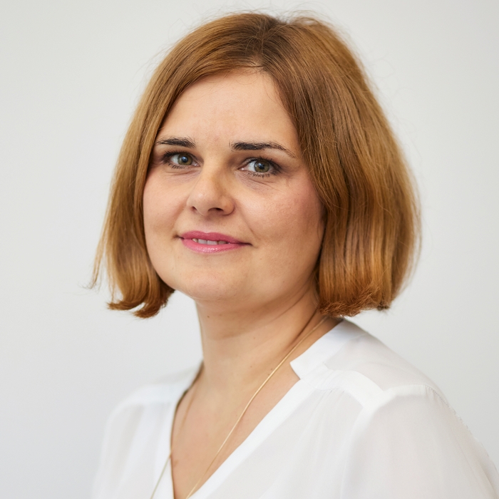 A woman with shoulder-length light brown hair wearing a white blouse. She is smiling softly at the camera.