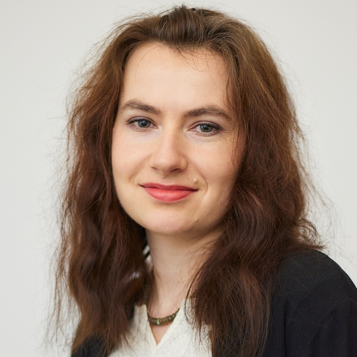 A professional headshot of a smiling woman with wavy brown hair. She is dressed in business attire, conveying a confident and friendly demeanor.
