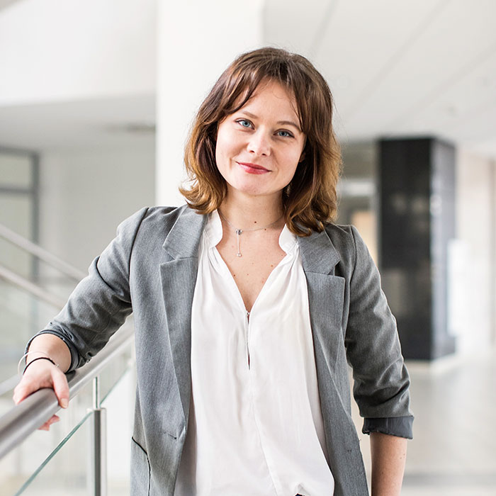 A woman in a business suit confidently stands on a railing, showcasing her professional demeanor and poise.