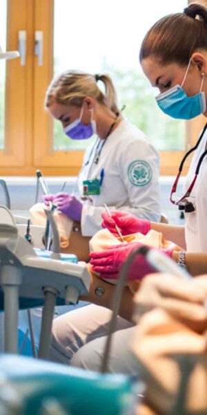 Several women in white coats and masks are engaged in work around a dental chair, demonstrating teamwork in a clinical setting.