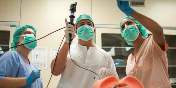 Three medical professionals in scrubs and masks attend to a patient on an operating table in a clinical setting.