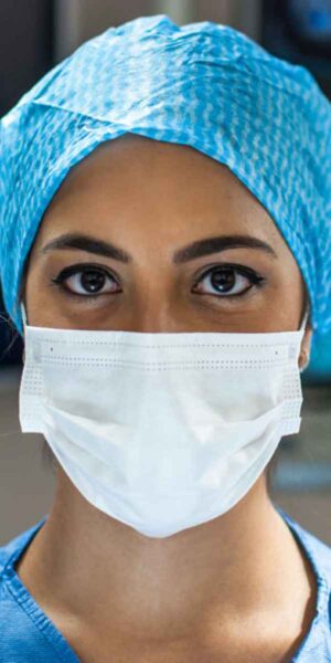 A woman dressed in scrubs and a surgical mask is poised for action in a healthcare facility, emphasizing safety and professionalism.