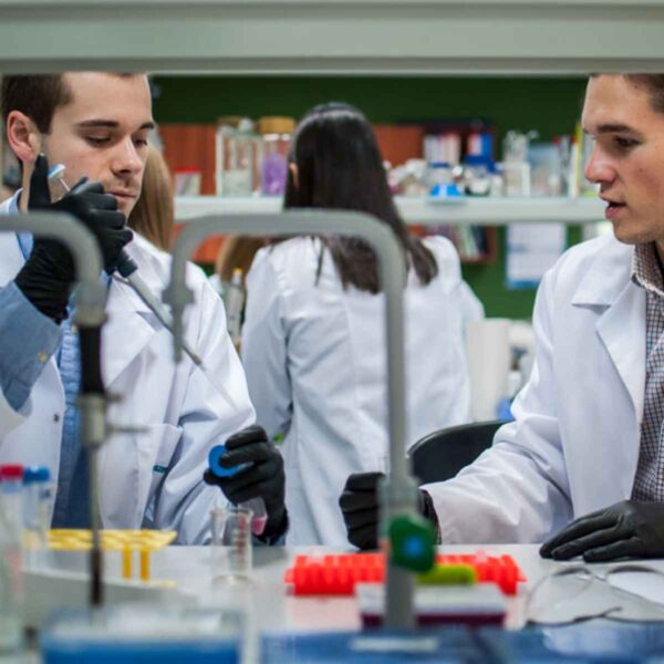 Two men wearing lab coats engage in a project, demonstrating teamwork and dedication in a laboratory setting.