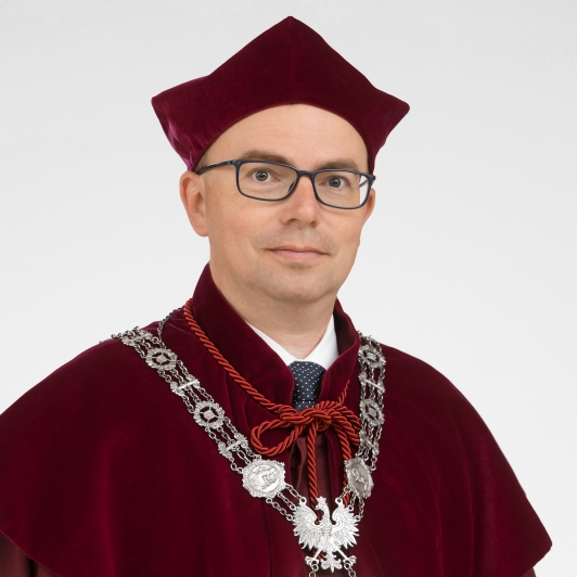 A man in a red robe and glasses stands confidently, embodying a scholarly presence in a formal setting.