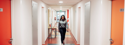 A woman confidently walks down a well-lit office hallway, surrounded by modern decor and glass-paneled offices.