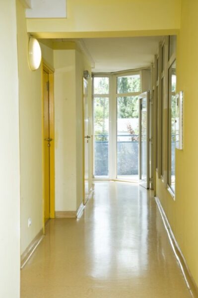 A brightly lit hallway with yellow walls, leading to a set of glass doors that open to an outdoor area.