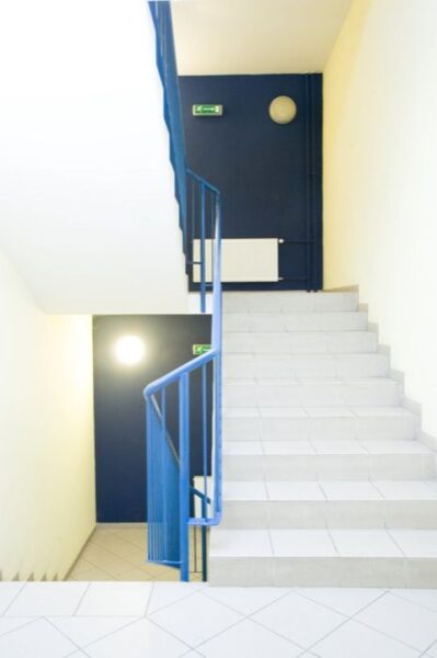 A stairwell with blue railings and white tiled steps. The walls are painted in a combination of blue and yellow.