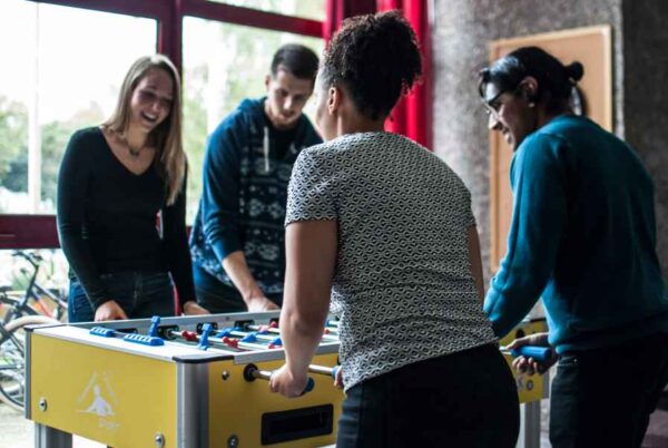 People enjoying a competitive foosball match in a bright room featuring expansive windows.