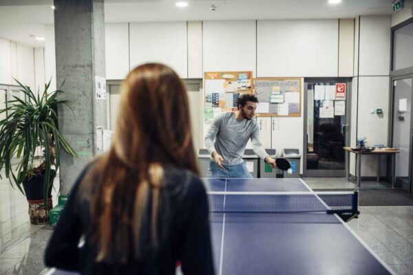 A man and woman playing ping pong together in an office, showcasing teamwork and leisure in a professional space.