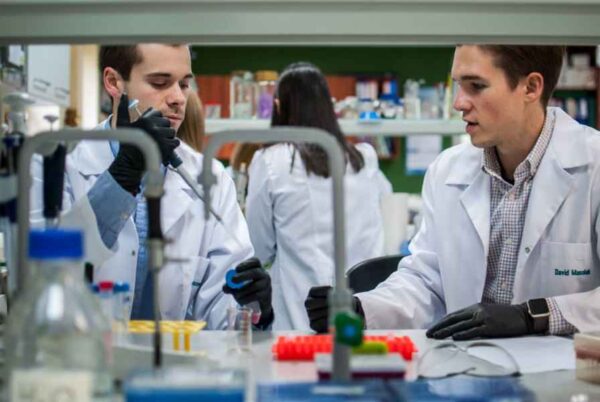 Two men wearing lab coats engage in a project, demonstrating teamwork and dedication in a laboratory setting.