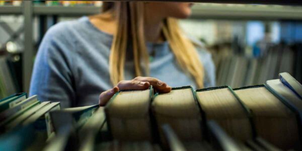 A woman browsing through bookshelves in a library, surrounded by rows of books and a serene atmosphere.