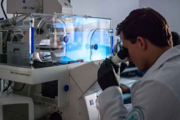 A male researcher in a lab coat focuses on a microscope, highlighting the process of scientific investigation.