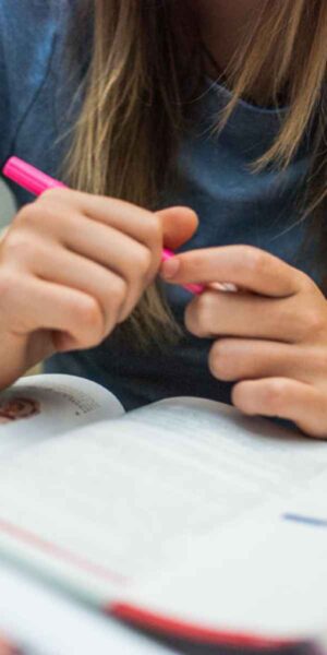 A girl is engaged in writing in a book with a pink pen, reflecting her imagination and dedication to her work.