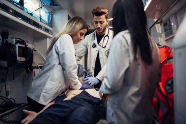 A closer look inside the ambulance simulation, where three medical students in lab coats practice emergency response techniques on a medical dummy. They are administering care in a focused and collaborative environment.