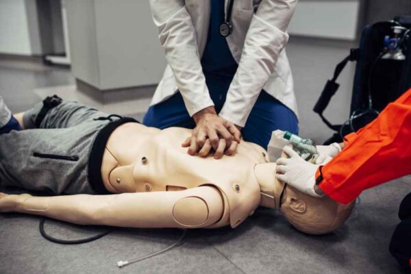 A simulated CPR session, where a student performs chest compressions on a dummy while a paramedic assists with maintaining the airway. The scenario highlights hands-on training in emergency response.