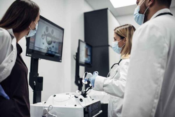 A group of medical students huddled around a simulation device, working together on laparoscopic surgical practice. The training is happening in a highly modern, technologically equipped setting.