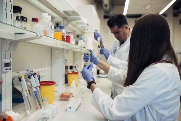 Medical students working in a laboratory, conducting various experiments. The students are wearing lab coats and gloves while handling pipettes and other laboratory equipment, focusing intently on their tasks.