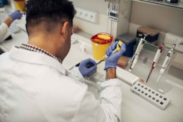 A close-up of a student in a laboratory setting, carefully using a pipette to transfer liquid into a test tube. The image captures the precision required in lab work.