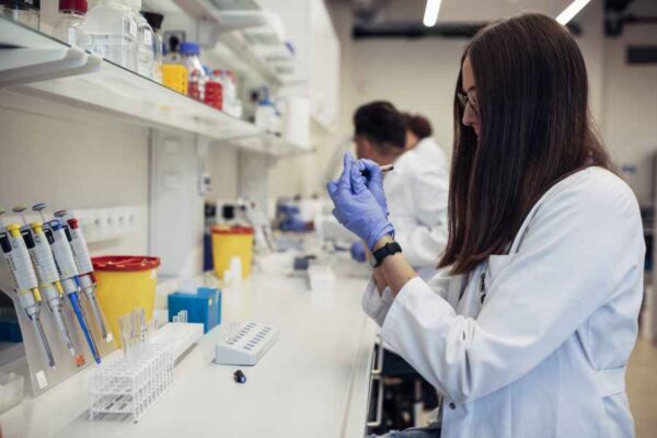 A student working in a laboratory, preparing a sample while surrounded by various lab instruments and containers. The environment is organized and equipped for detailed research tasks.
