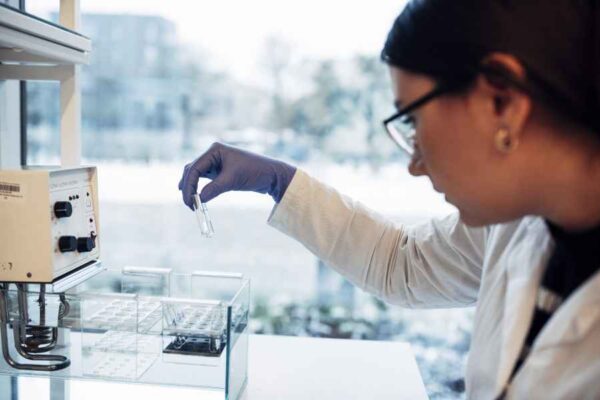 A focused laboratory setting where a student is analyzing a sample near a large window. The lab is equipped with various tools and instruments for research and experimentation.