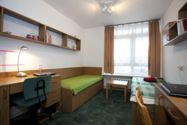 A compact room featuring a desk, a bed, and a window, creating a cozy and functional living space.