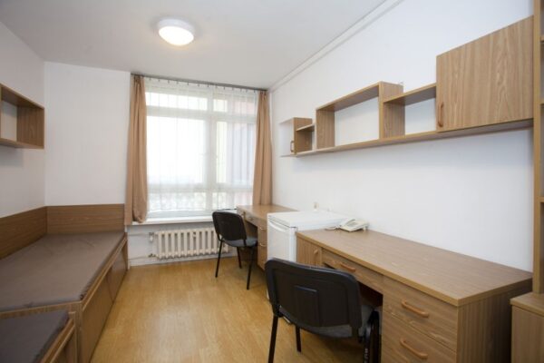 A compact room featuring a desk, a chair, and a bed, illustrating a simple and functional living space.