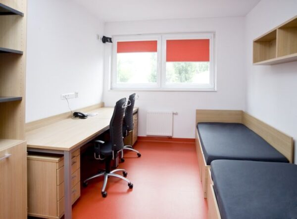 A room featuring a desk positioned between two neatly made beds, creating a cozy and functional living space.