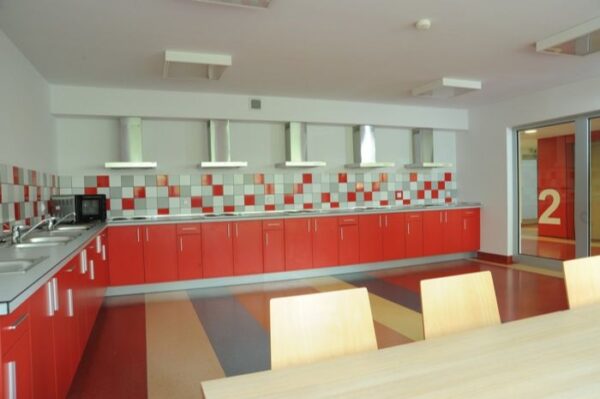 A modern kitchen featuring vibrant red cabinets and a central table, creating a warm and inviting atmosphere.