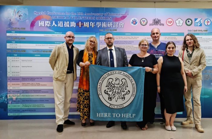 Color photo of posing conference participants holding a flag with PUMS logo and 