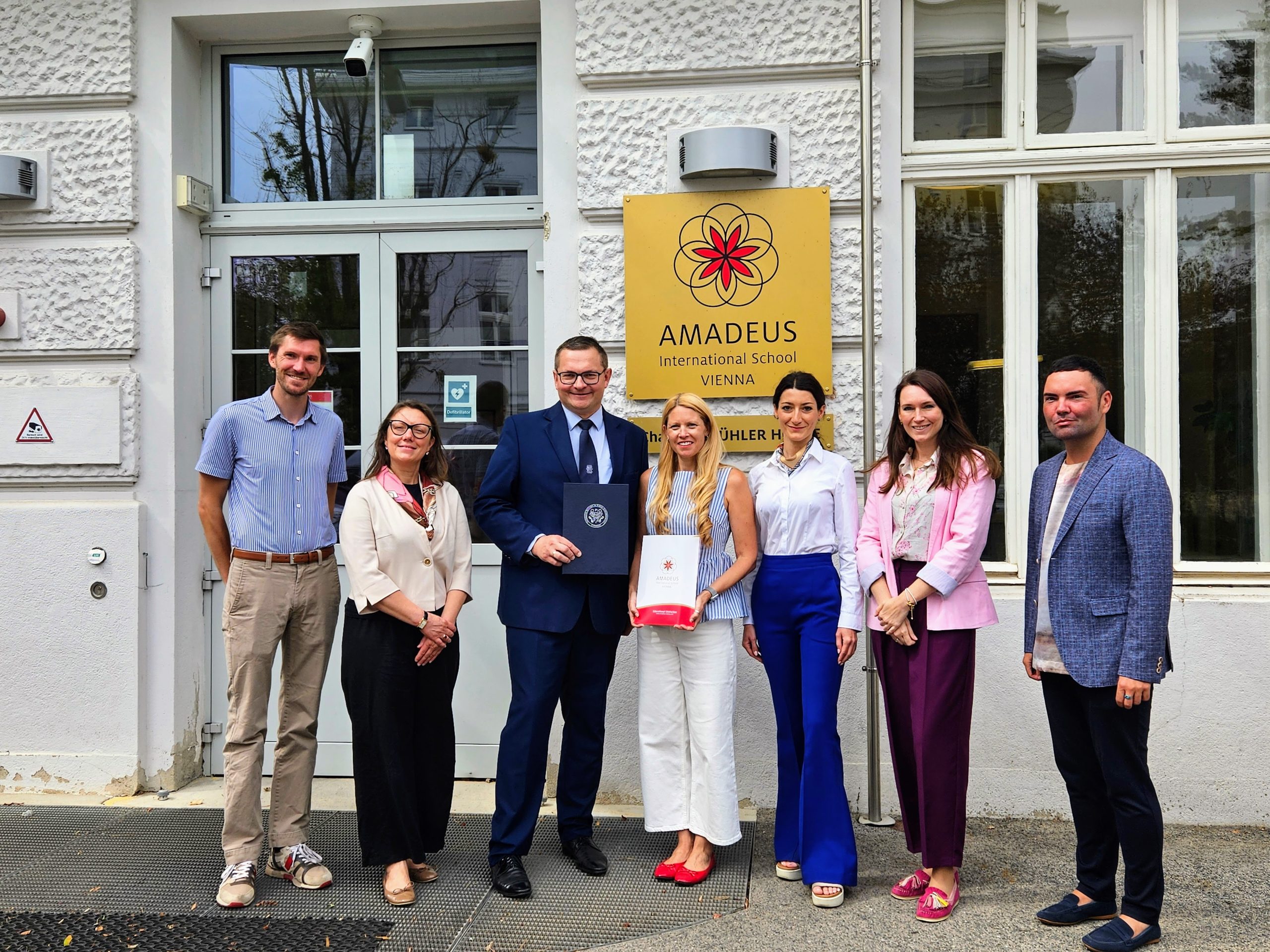 Group color photo showing delegates from PUMS and representatives of Amadeus standing in front of the school entrance